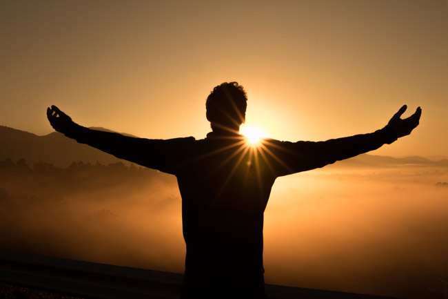A man in silhouette raises arms facing a sunrise